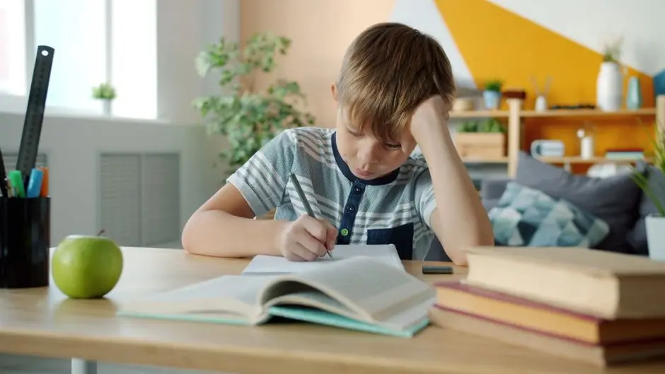 Seorang siswa belajar di meja kayu dengan buku dan laptop di kamar sederhana, menunjukkan semangat meraih sekolah favorit dari daerah
